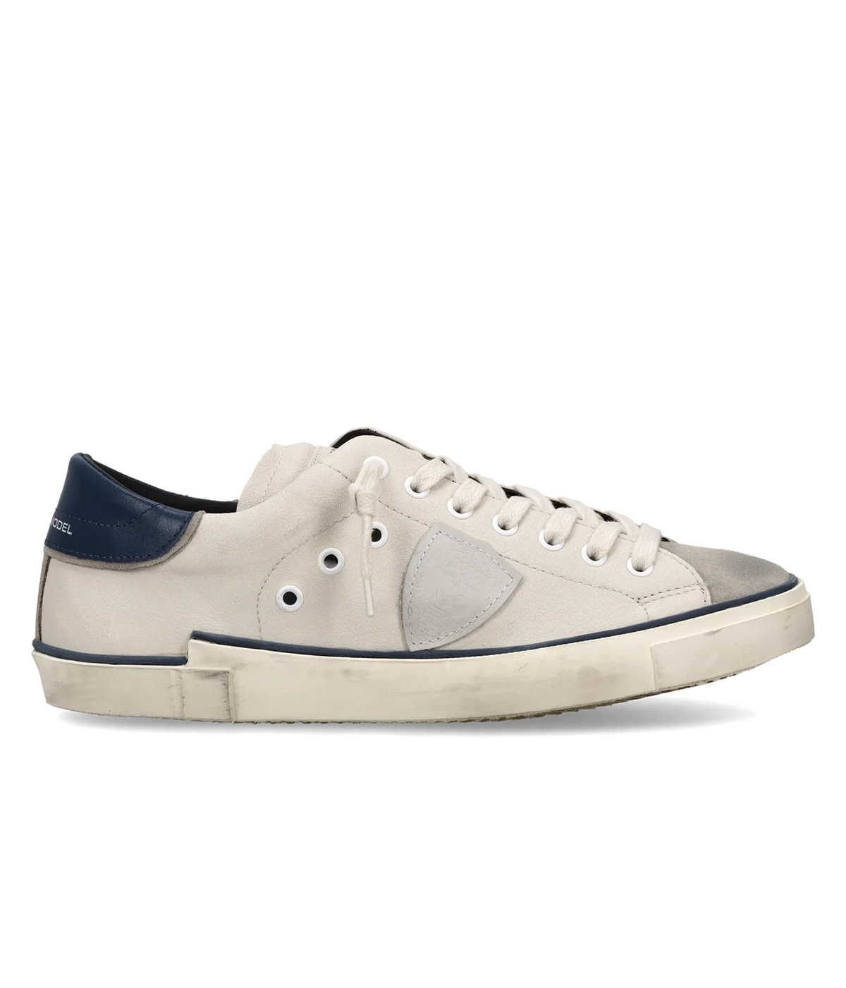 Side profile of the Philippe Model Prsx Low Man in Vintage Bordure Lait Bleu, showing the off-white leather upper, grey suede toe, side shield patch, navy heel tab and distressed sole with navy trim