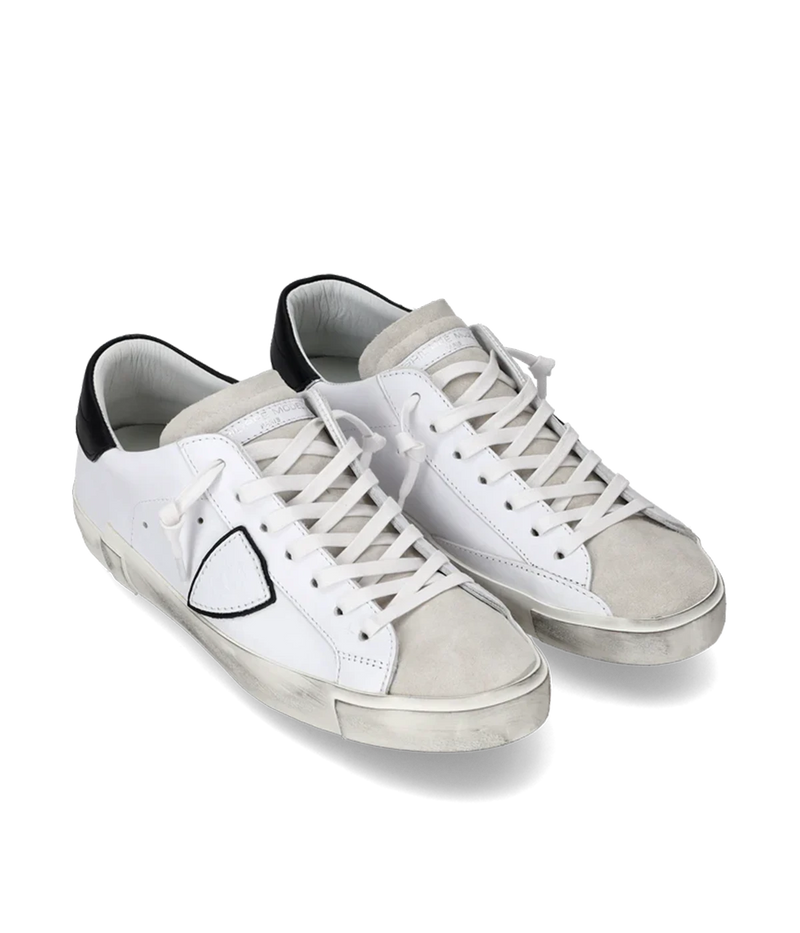 Angle view of Philippe Model PRSX Low Man sneakers, emphasizing the shield on the side of the shoe with the City of Paris coat of arms. The calfskin and suede upper has a worn, vintage-used effect, and the screen-printed laces add to the sneakers' timeless appeal.