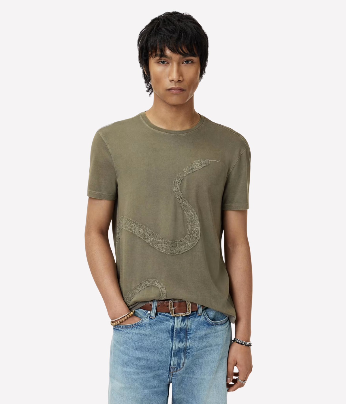 Man wearing an olive green t-shirt with a graphic design and blue jeans on a white background