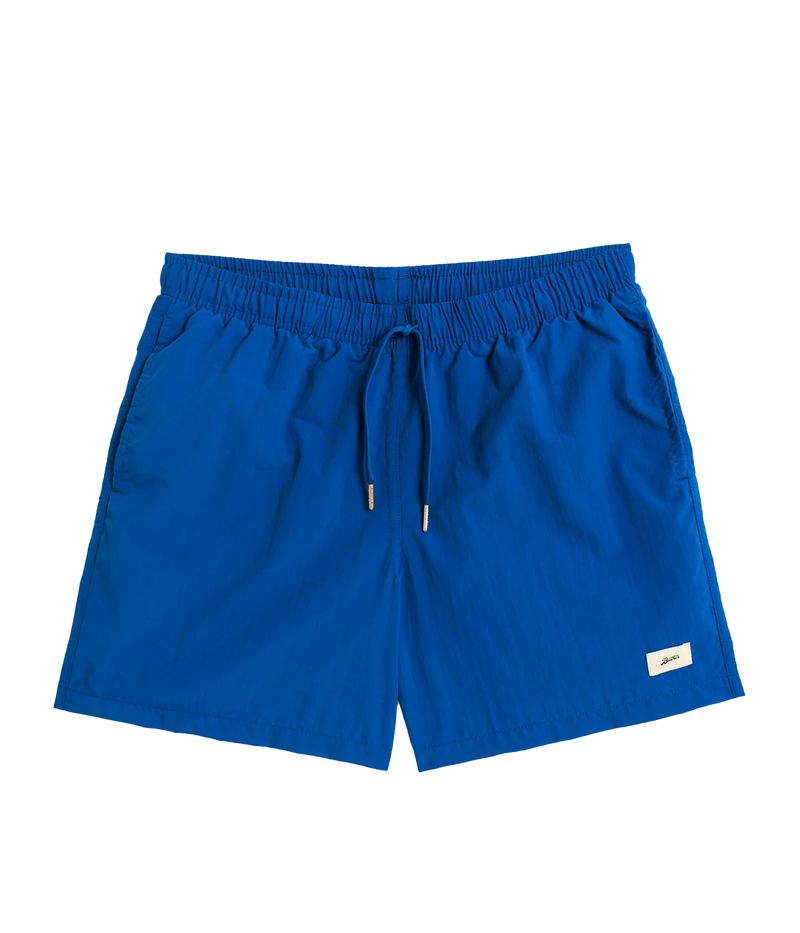 Front view of Bather solid swim trunks, featuring a 5.5-inch inseam and an elasticized waist for a secure and comfortable fit. Made from 100% recycled quick-dry polyester, the trunks are designed with reinforced side pockets and a back pocket with a snap closure.