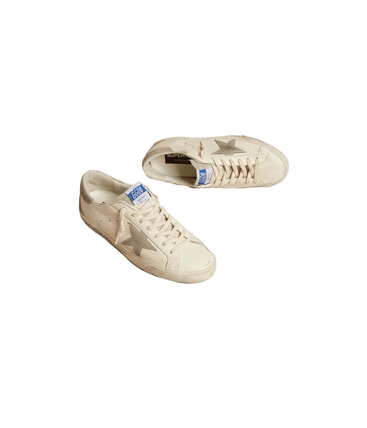 A pair of Golden Goose Super Star Sneakers in off-white calf leather with grey accents. The sneakers feature perforated detailing, a signature suede star patch on the sides, and a logo patch at the tongue. The contrasting grey branded heel counter adds an extra touch of style. Designed with a front lace-up fastening, round toe, and flat rubber sole for comfort and durability, these sneakers are perfect for casual everyday wear.