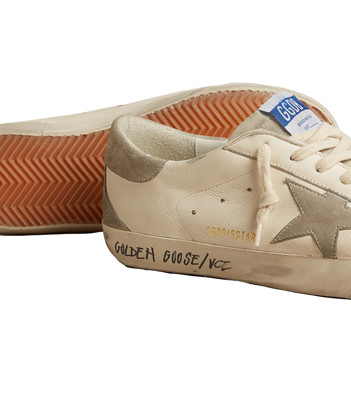A pair of Golden Goose Super Star Sneakers in off-white calf leather with grey accents. The sneakers feature perforated detailing, a signature suede star patch on the sides, and a logo patch at the tongue. The contrasting grey branded heel counter adds an extra touch of style. Designed with a front lace-up fastening, round toe, and flat rubber sole for comfort and durability, these sneakers are perfect for casual everyday wear.