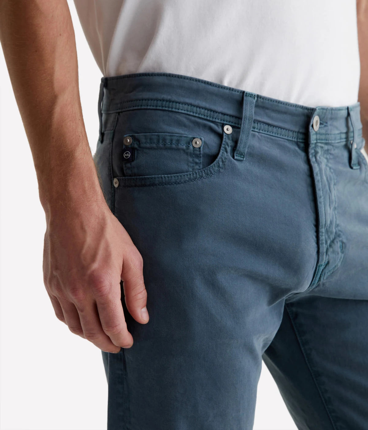 AG Tellis Slim Fit pants in a sulfur-dyed dark blue shade, featuring a fitted upper block and tapered leg. Crafted from lightweight Sueded Stretch Sateen from Italy, these five-pocket men's pants offer refined style and exceptional comfort. Measurements include a 10" front rise, 15 3/4" knee opening, 13 3/4" bottom opening, and 34" inseam.
