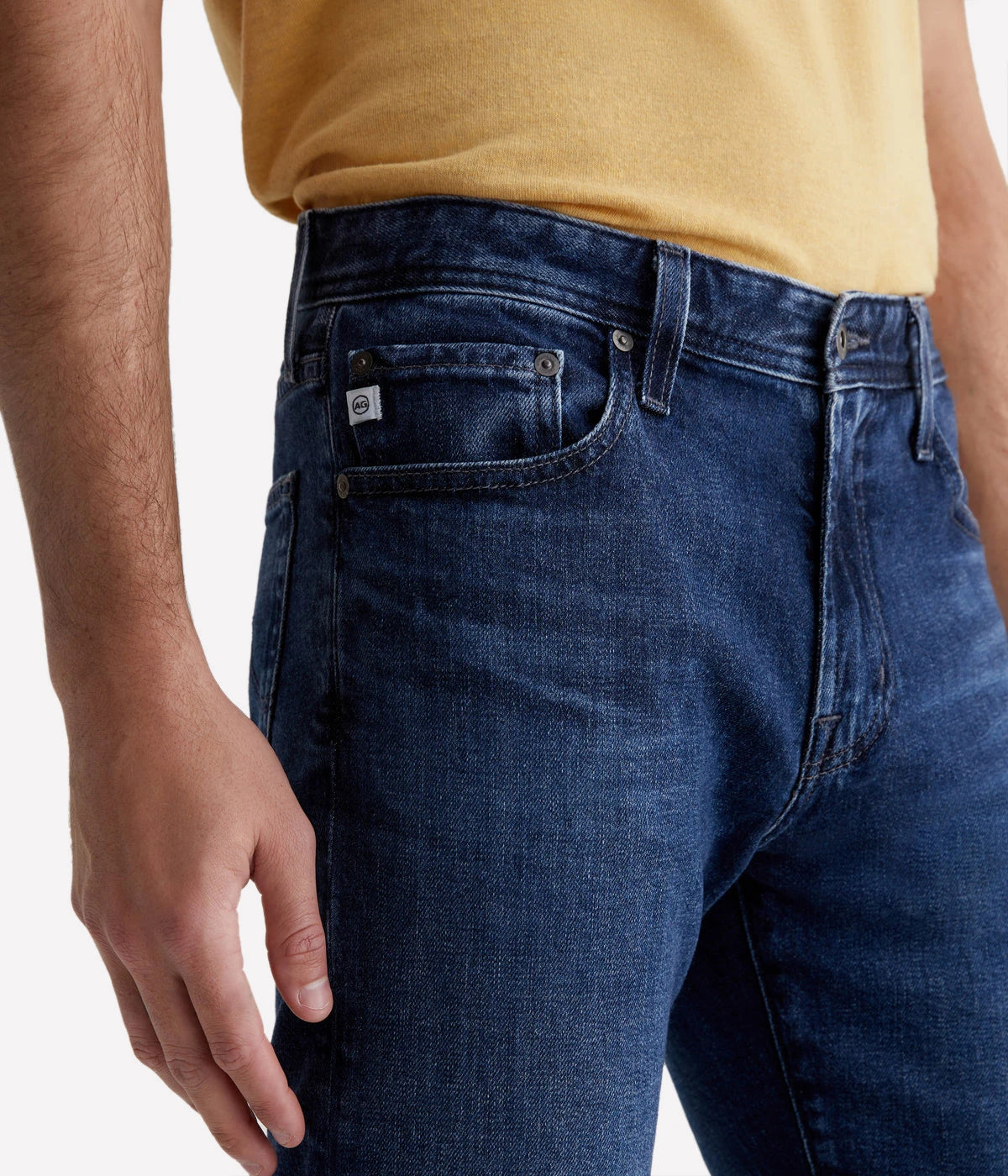 The Tellis Modern Slim Jean displayed in a dark indigo wash, showcasing fading and whiskering, with a slim fit cut and tapered leg opening.