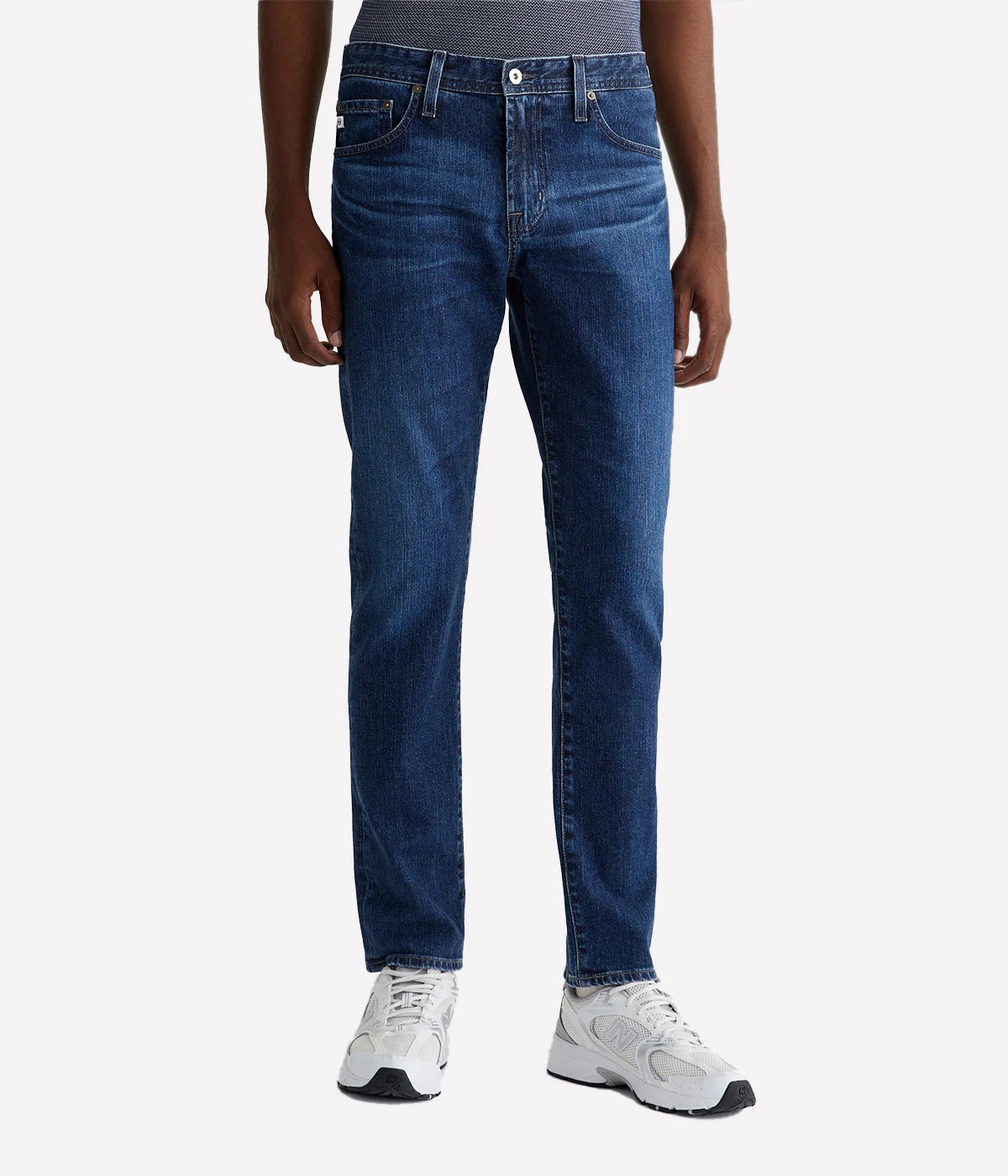AG Tellis slim-fit jeans for men in a medium indigo wash, featuring a fitted upper block and tapered leg opening. Crafted from 11 oz. Lead Denim with stretch, finished with a biodegradable cellulose patch at the back waistband.