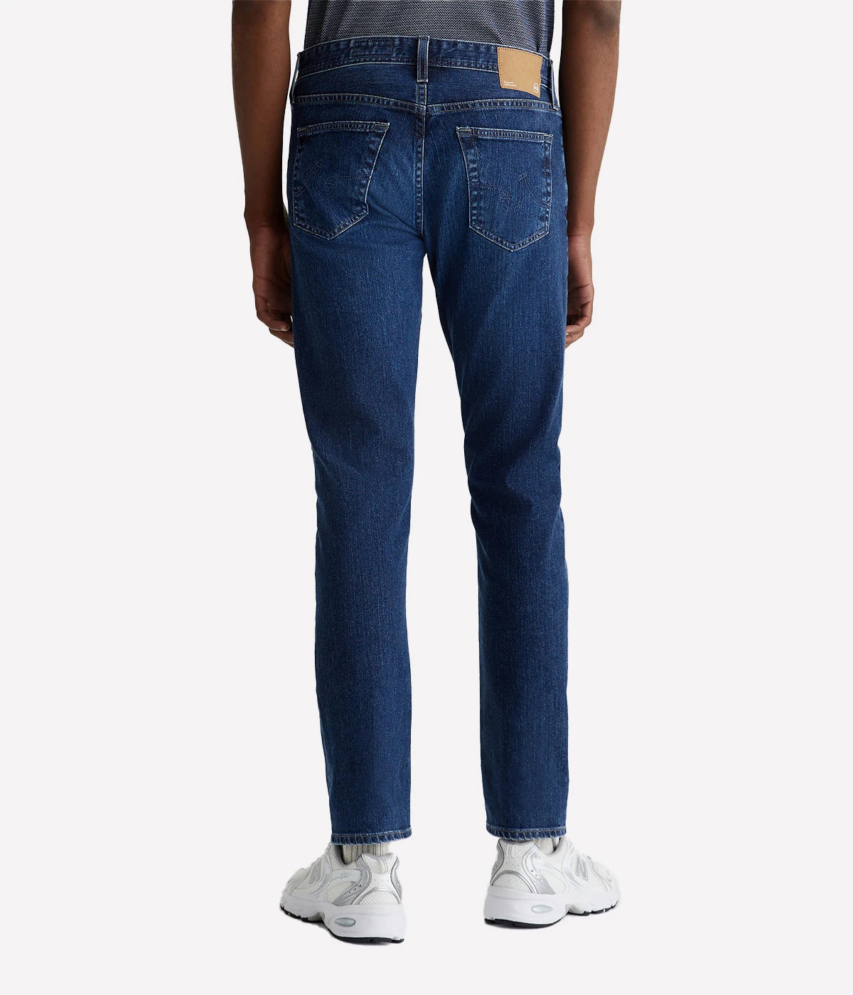 AG Tellis Modern Slim Jeans for men in a medium indigo wash, created using eco-friendly AG Vapor Wash™ technology for a sustainable finish. Designed with a fitted upper block and tapered leg opening, these jeans are crafted from 11 oz. Lead Denim with comfortable stretch. Complete with a vegan, biodegradable cellulose patch at the back waistband for a conscious style choice.