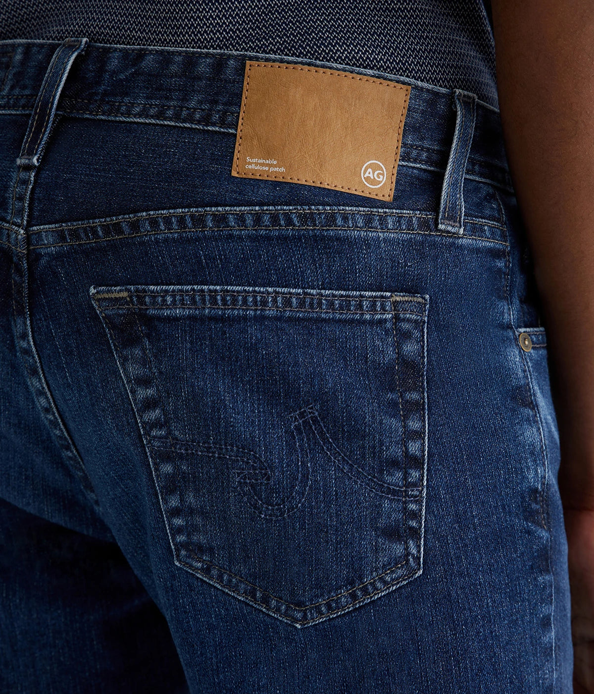 AG Tellis Modern Slim Jeans for men in a medium indigo wash, created using eco-friendly AG Vapor Wash™ technology for a sustainable finish. Designed with a fitted upper block and tapered leg opening, these jeans are crafted from 11 oz. Lead Denim with comfortable stretch. Complete with a vegan, biodegradable cellulose patch at the back waistband for a conscious style choice.