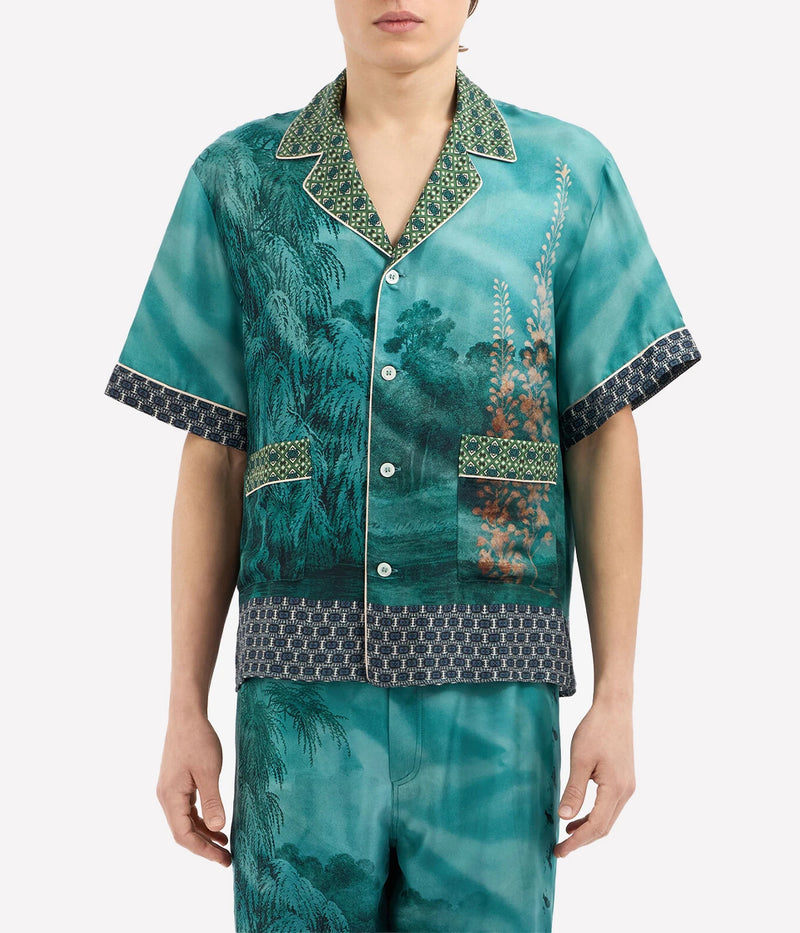 Short-sleeved silk shirt with teal landscape, botanical, and bird motifs, open collar, and button front.