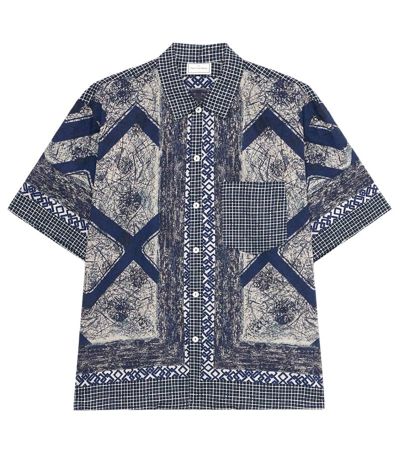 Short-sleeved cotton shirt featuring navy and cream patchwork design with chevron, grid, and abstract patterns, chest pocket, and relaxed fit.