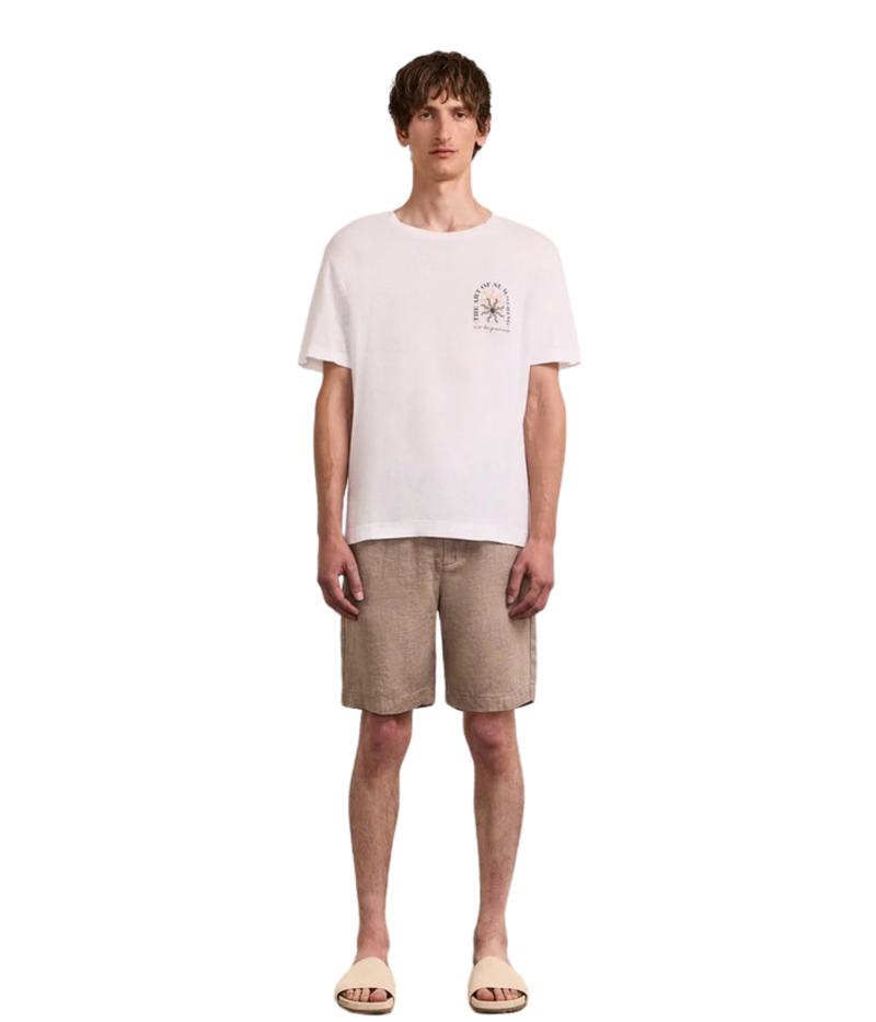 Man wearing a white t-shirt with a small graphic and beige shorts on a white background