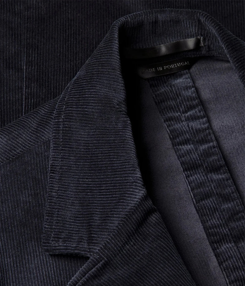 Close-up of a dark navy corduroy jacket with a visible collar and inner lining, showing a small black neck label that reads 'MADE IN PORTUGAL'.