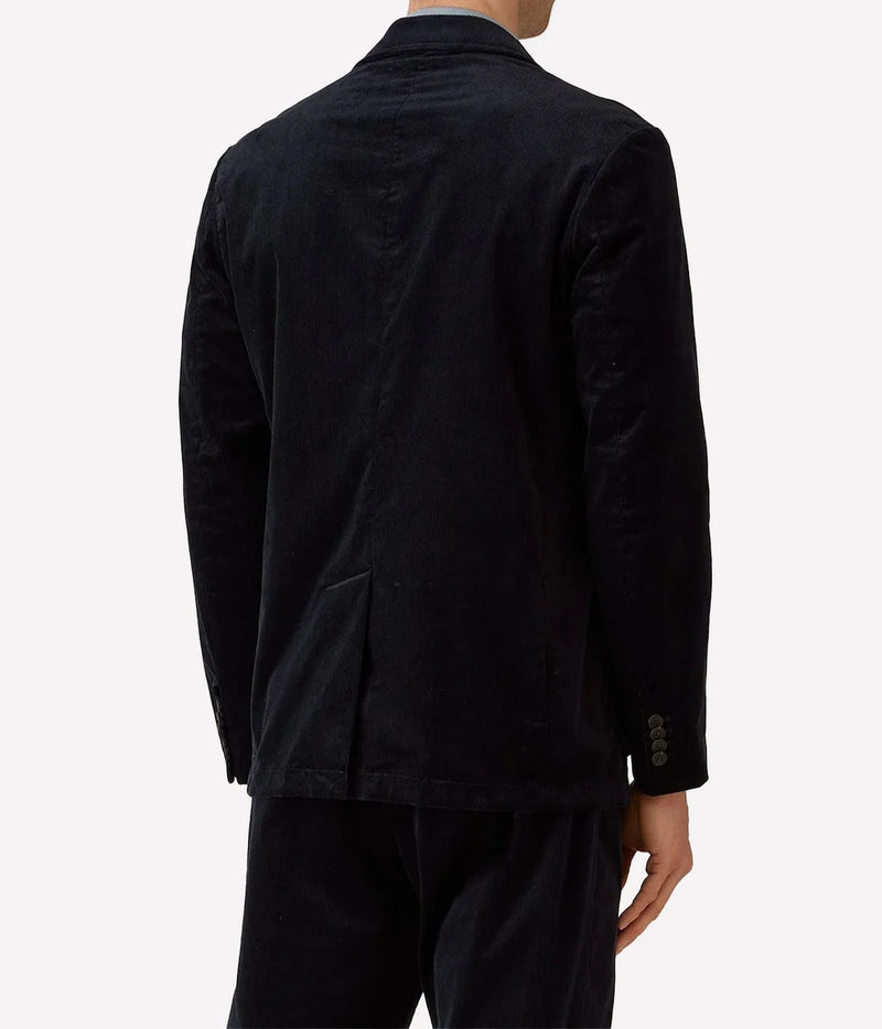 Rear view of a person wearing a dark navy corduroy blazer and matching trousers against a light gray studio background.