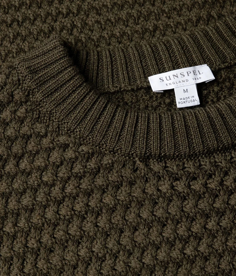 Close-up of a ribbed knit sweater collar with a visible Sunspel label reading England No. 12 and size M, shown against the textured knit body.