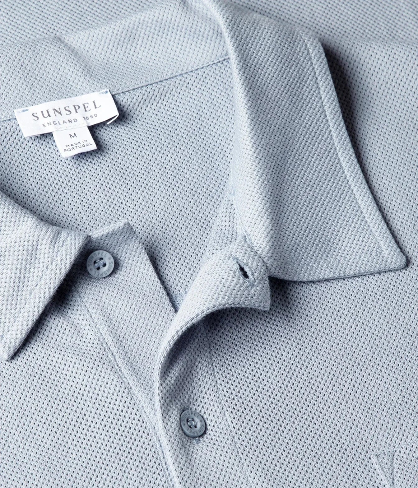 Close-up of a light blue textured polo shirt collar with a visible SUNSPEL label and matching buttons.
