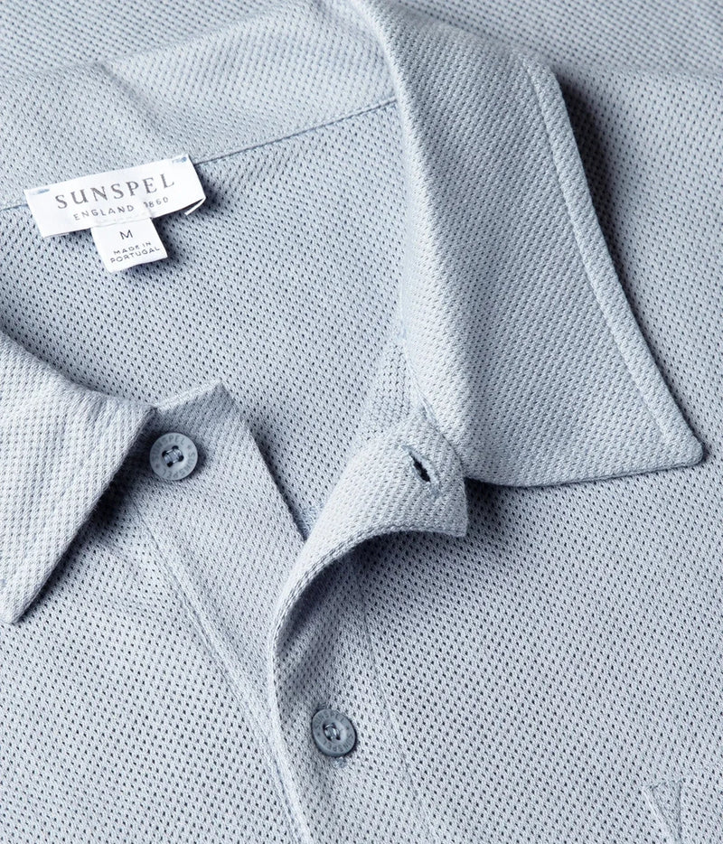 Close-up of a light blue textured polo shirt collar with a visible SUNSPEL label and matching buttons.