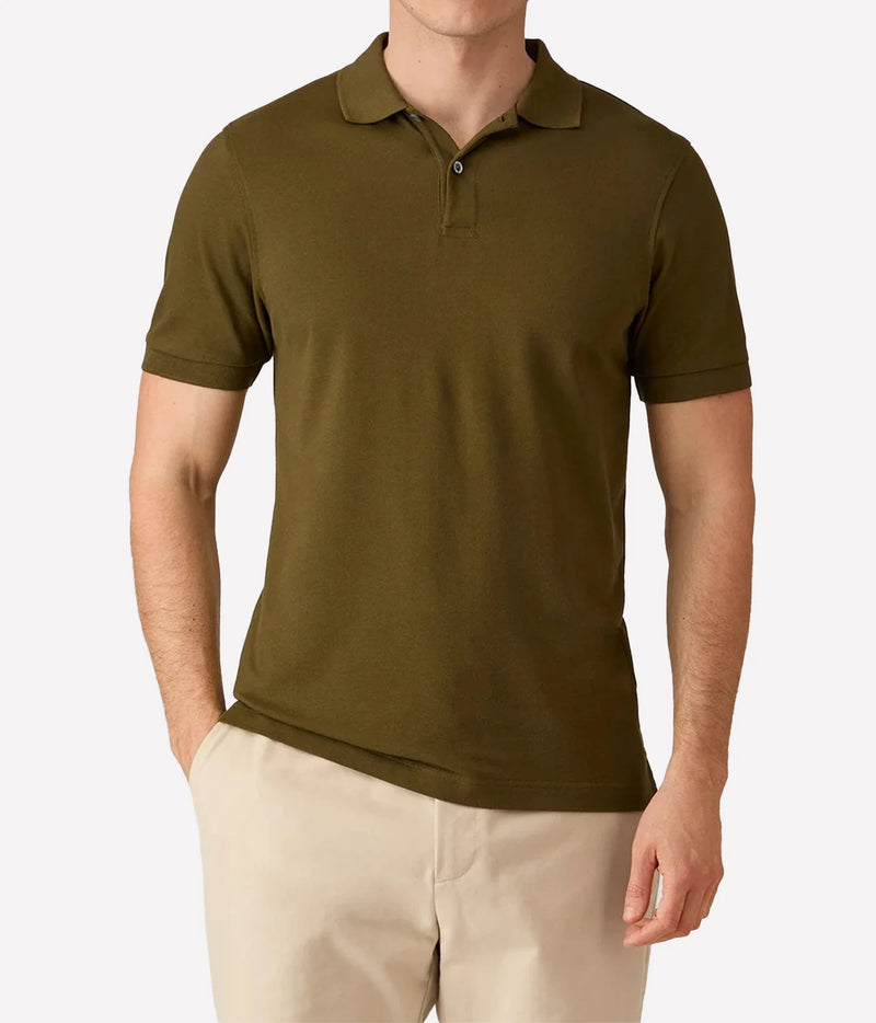 A man wearing a short-sleeve polo shirt in olive green, paired with beige pants, shown from the waist up against a light gray background.