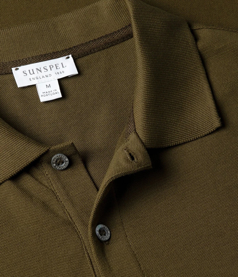 Close-up of a collared knit polo shirt in olive green with a visible SUNSPEL England 1885 neck label and dark buttons.