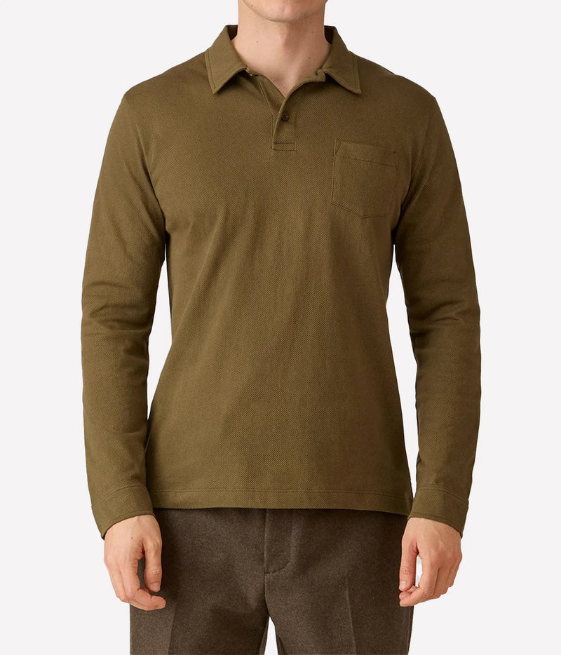 A man wearing a long-sleeve olive green polo shirt with a chest pocket, paired with brown trousers, shown against a plain light gray background.