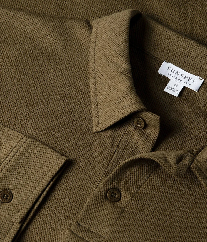 Close-up of a textured olive green polo shirt collar with a visible white inner neck label reading SUNSPEEL ENGLAND MADE.