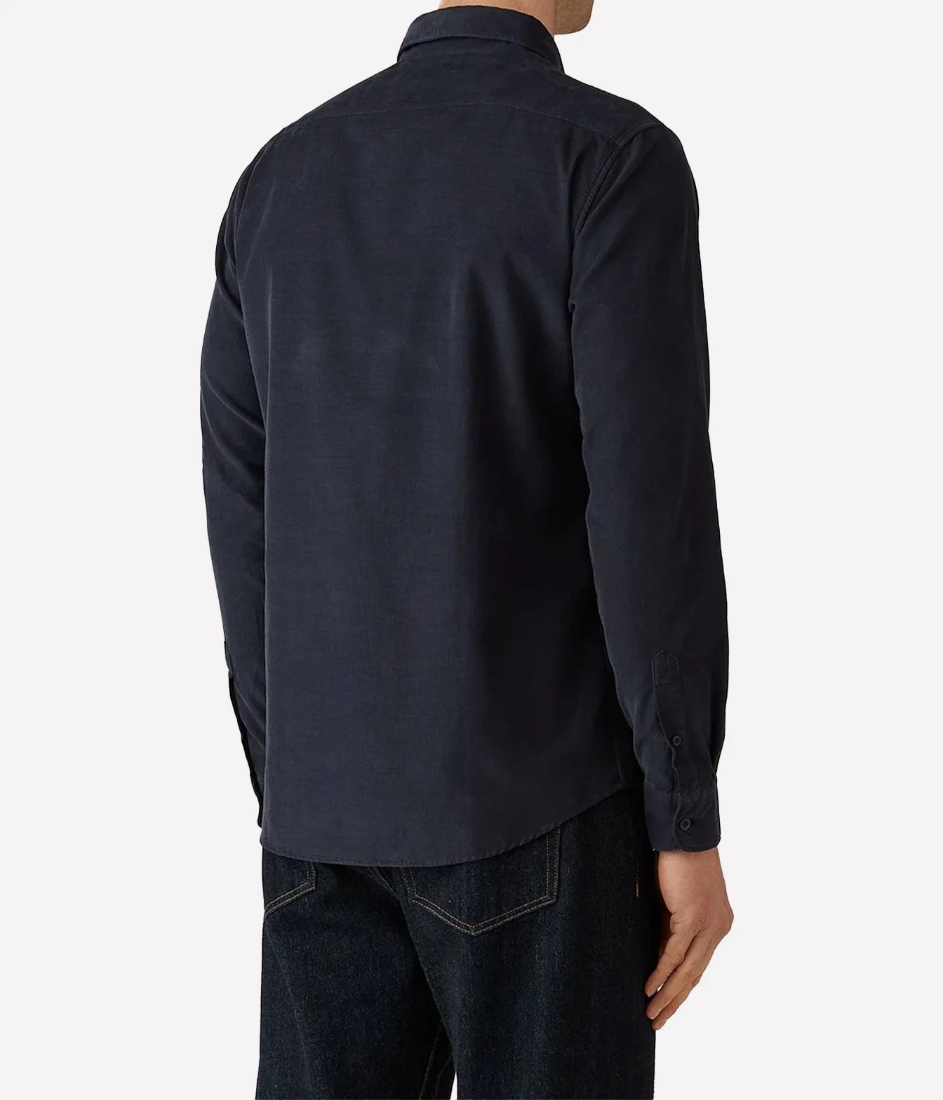 A man wearing a dark navy blue long-sleeve button-down shirt, shown from the back, paired with dark jeans against a light gray studio background.