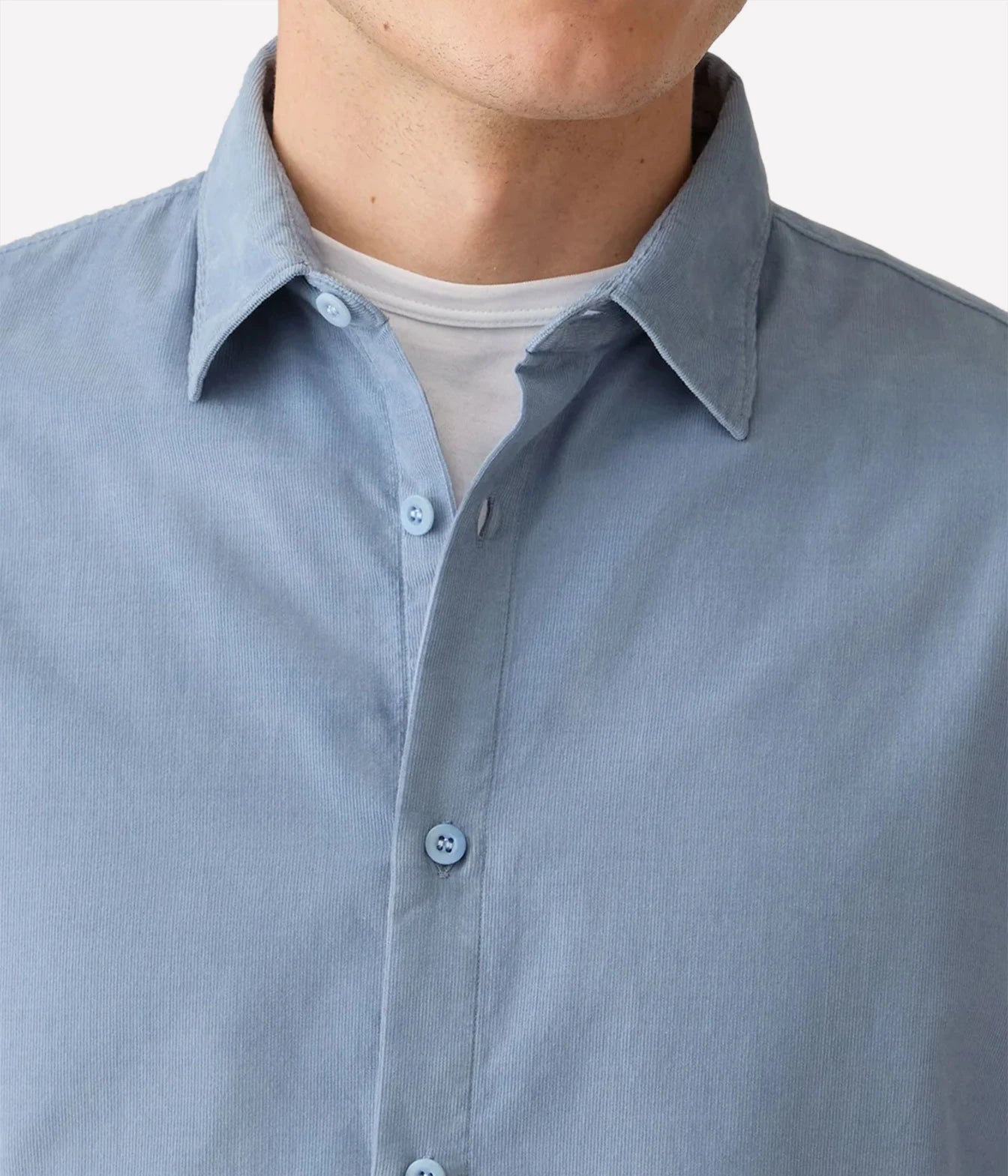 Close-up of a man wearing a light blue button-down shirt over a white t-shirt, showing the collar, buttons, and fabric texture.