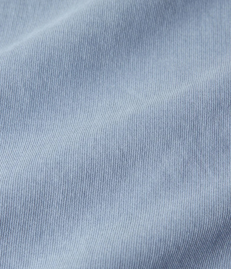 A close-up of light blue ribbed fabric texture with soft folds and a fine knit pattern.