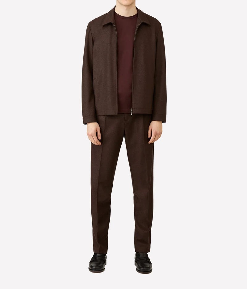 A model wearing a dark brown jacket and matching trousers over a burgundy t-shirt and black shoes, photographed against a solid light gray background.