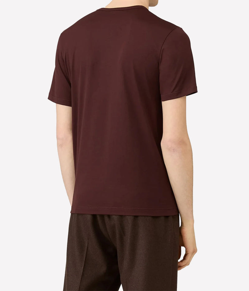 A man viewed from the back wearing a dark burgundy short-sleeve t-shirt and dark brown pants, set against a plain light gray background.