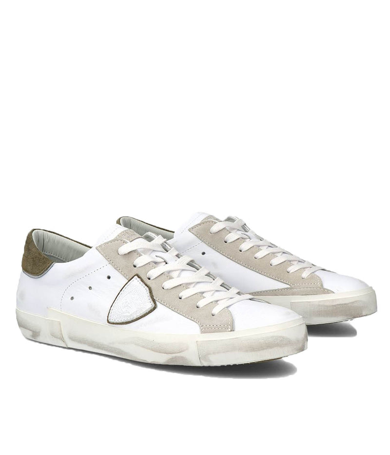 Angle view of Philippe Model PRSX Low Man sneakers, emphasizing the shield on the side of the shoe with the City of Paris coat of arms. The calfskin and suede upper has a worn, vintage-used effect, and the screen-printed laces add to the sneakers' timeless appeal.